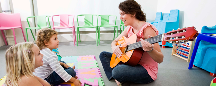 Image of two young students listening to teacher with guitar