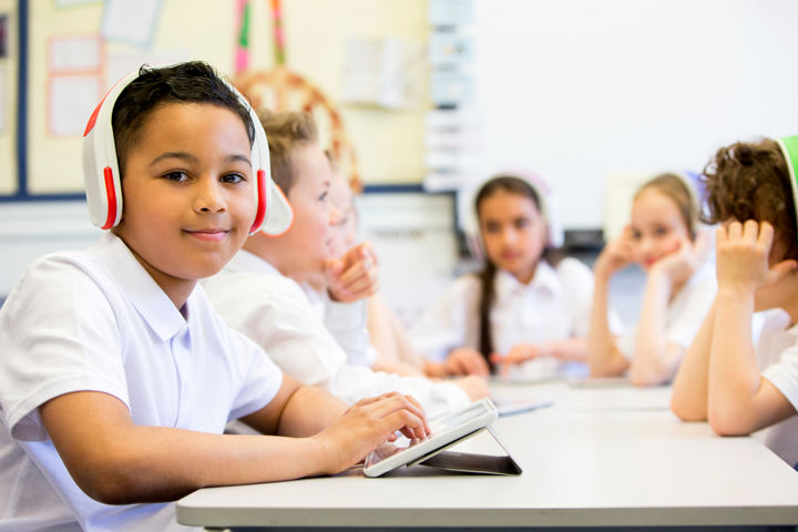 Image of boy with headphones and a tablet with other students in the background