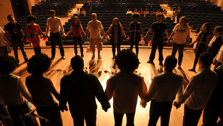 Students in circle on stage holding hands