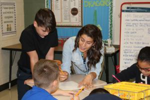 female teacher explaining something to children at a table